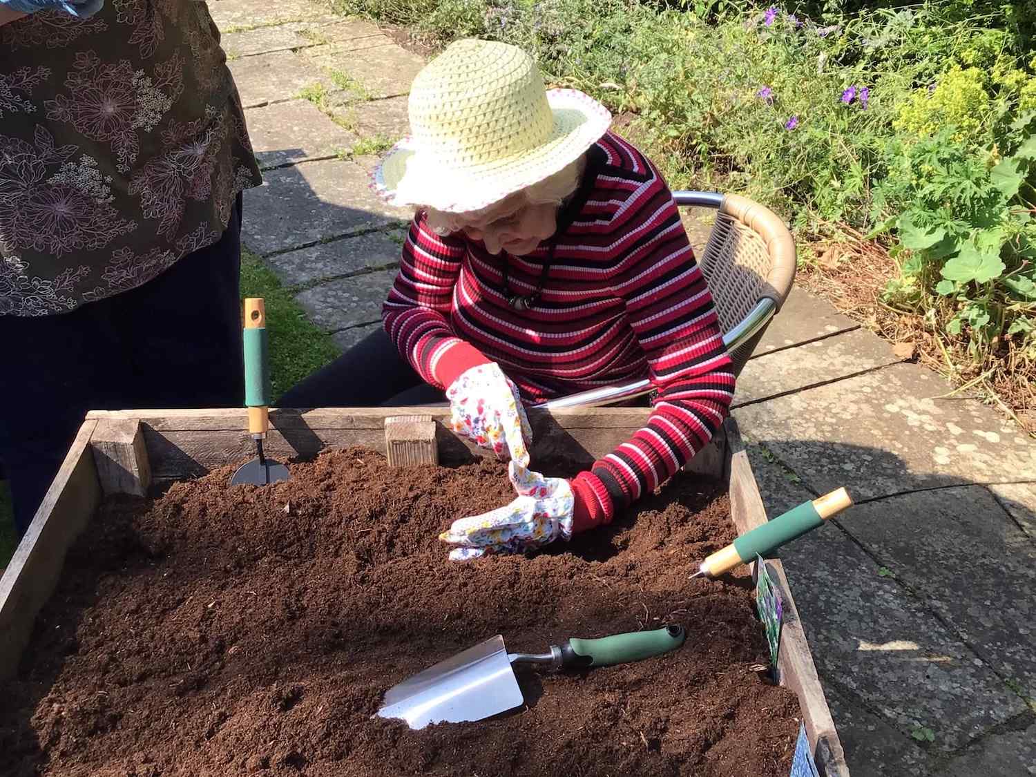 Elderly woman wearing gloves and hat planting seeds in dirt