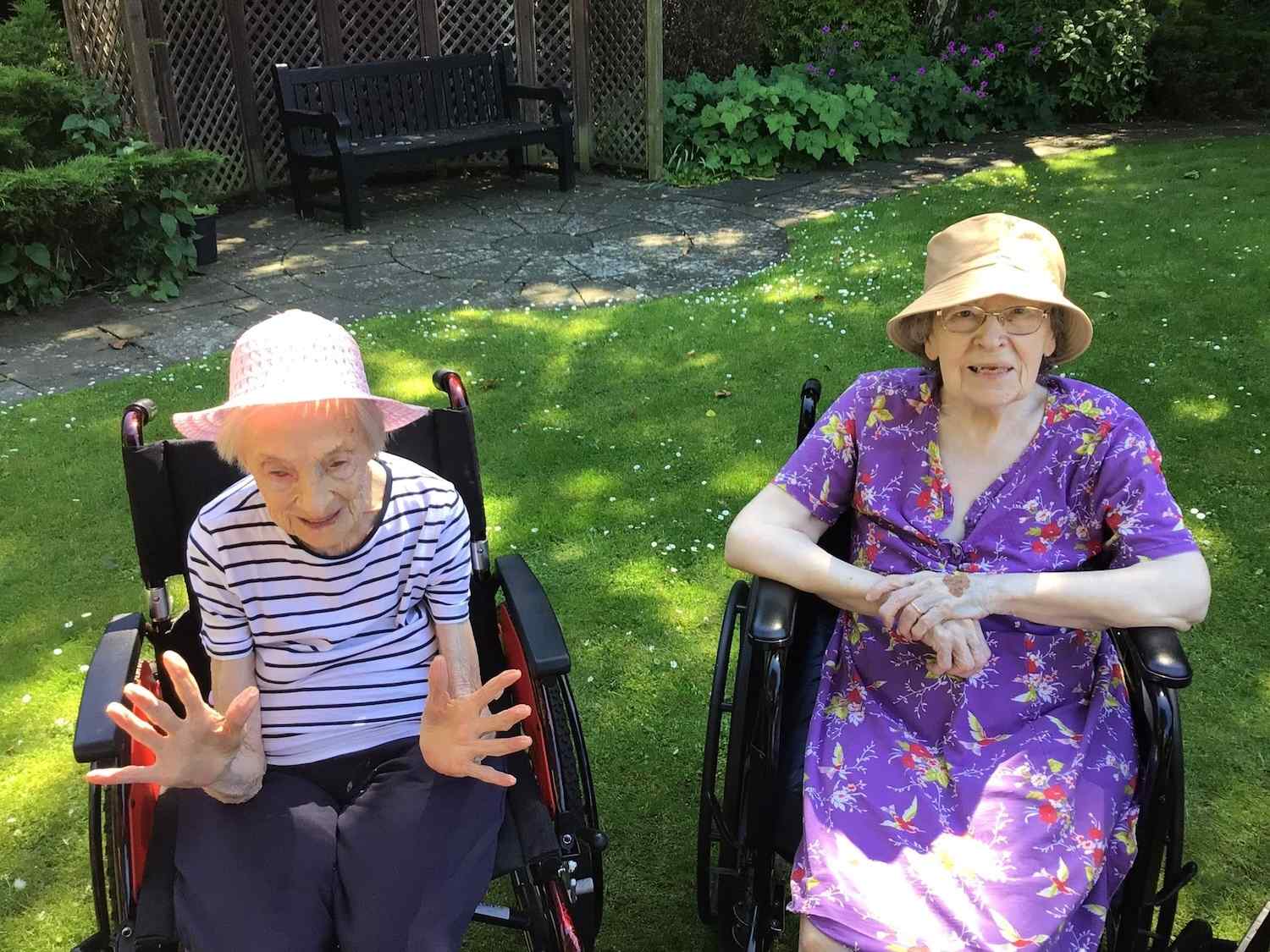 Two elderly women in wheelchairs smiling in sun hats